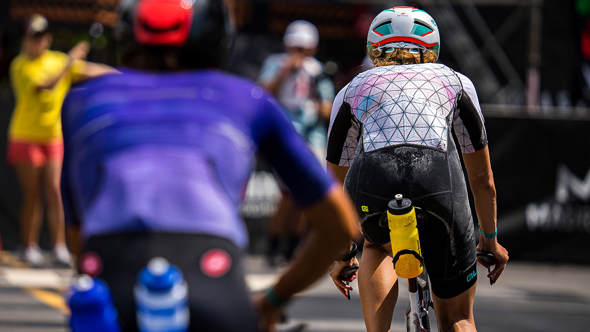 Ironman World Championships Hawai’i 2022 Woman With Sweat Stains On Their Triathlon Suits Ride Their Bikes Into Transition 2 During A Race In Kona